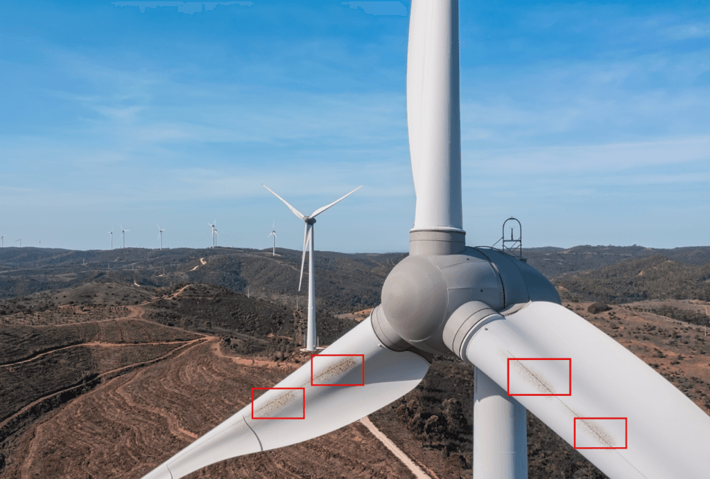 Close-up of wind turbine blades with yellow residue, overlooking a hilly landscape with distant turbines.